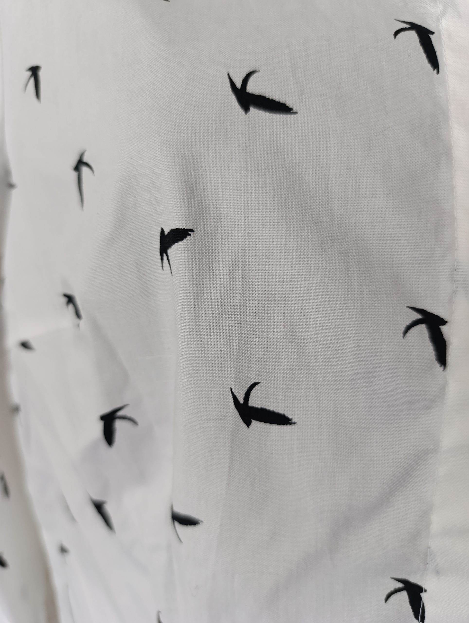 Détail du tissu en coton blanc avec imprimé oiseaux (hirondelles).